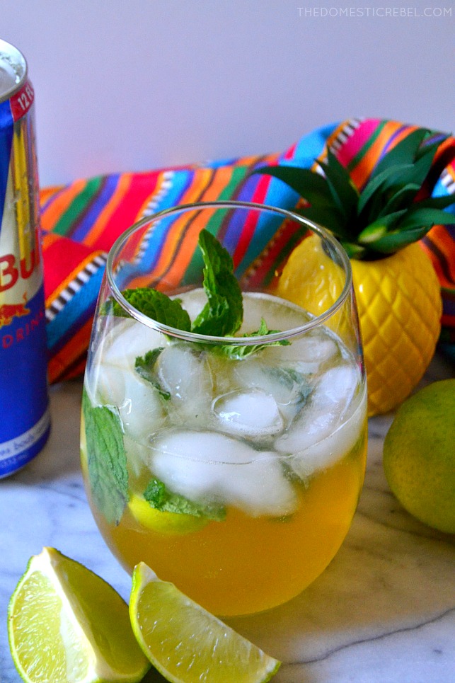 red bull pina cocojito in clear glass with pineapple statue, lime wedges