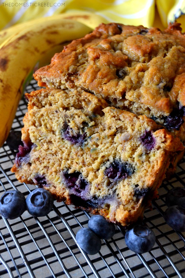 blueberry banana bread sliced loaf on wire rack with bananas and blueberries