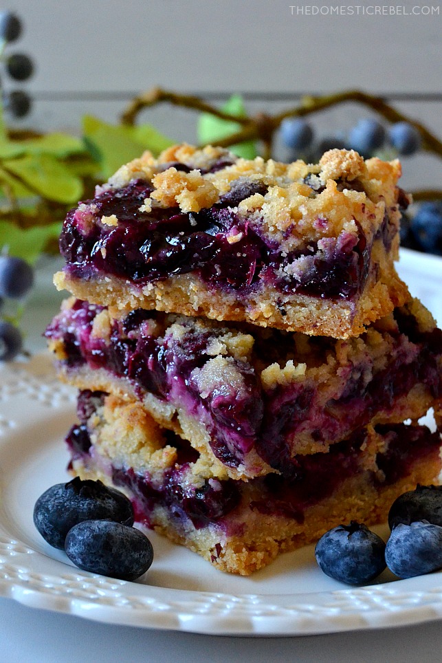 closeup stack of blueberry crumb bars on white plate with fresh blueberries
