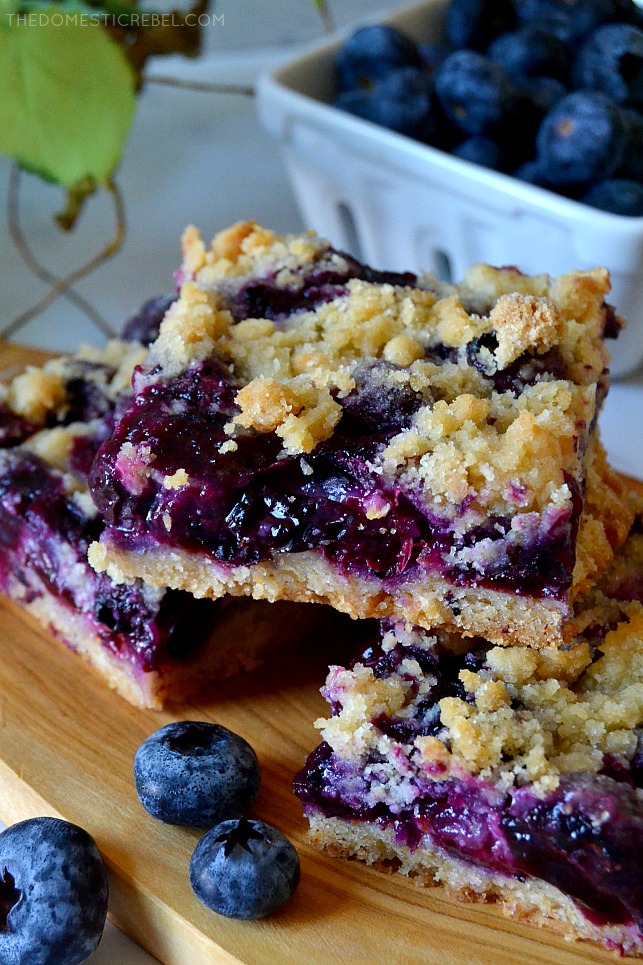 closeup of blueberry crumb bars arranged on wooden plank with blueberries