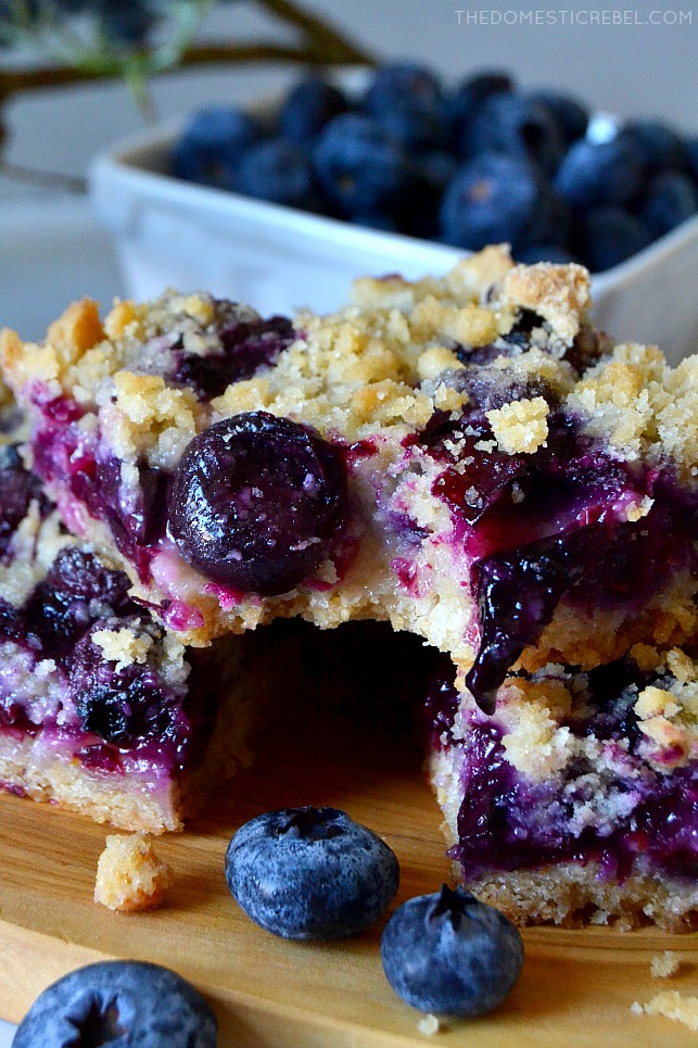 blueberry crumb bars with bite missing on wooden plank and blueberries in background
