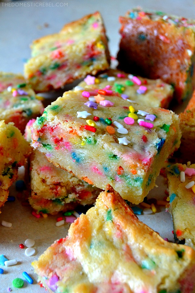 cake batter blondies arranged in a pile on wood with sprinkles