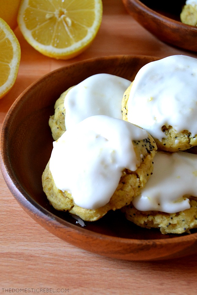 closeup of lemon poppyseed cookies on wooden plate with lemon wedges