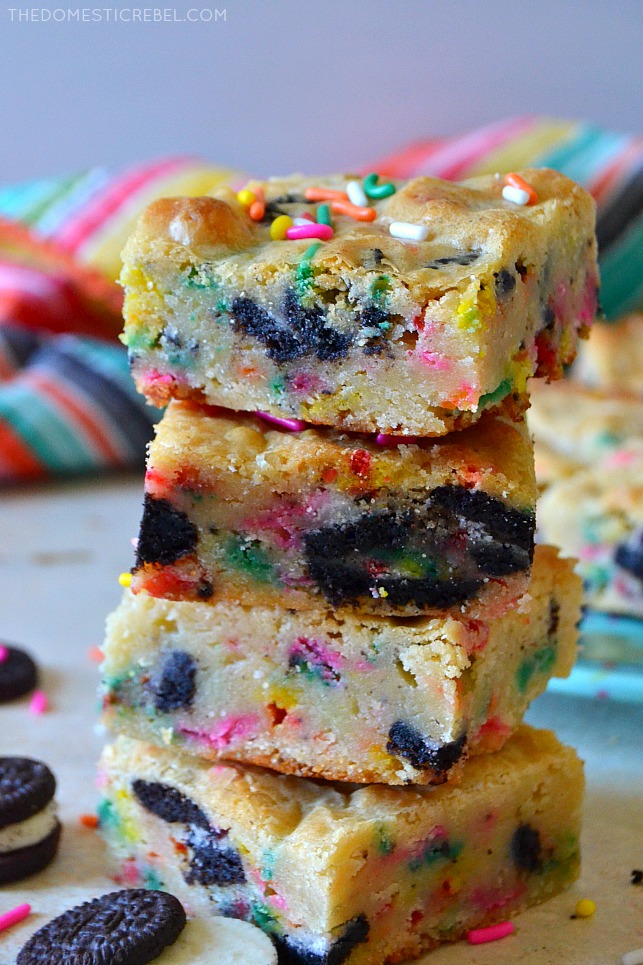 Four cookies & cream cake batter blondies stacked on white wood with oreo cookies