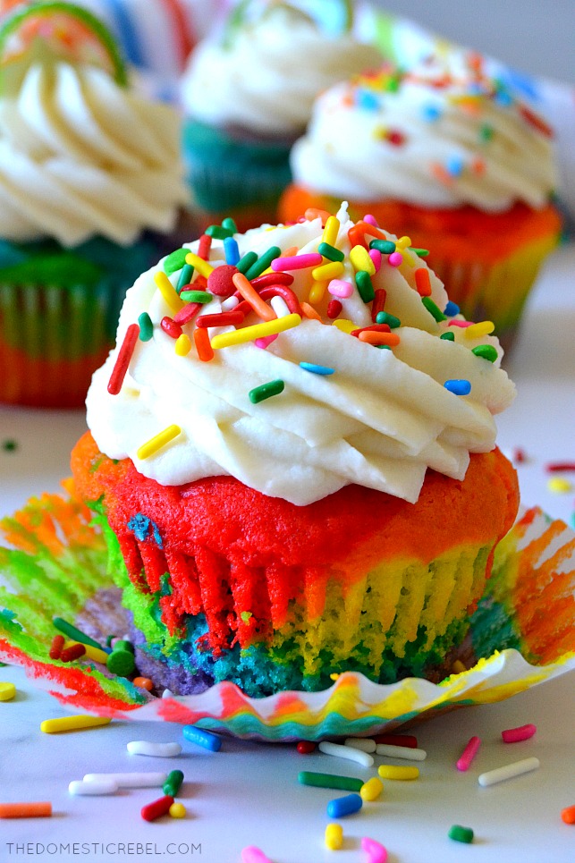 Rainbow cupcake in wrapper on white background with sprinkles