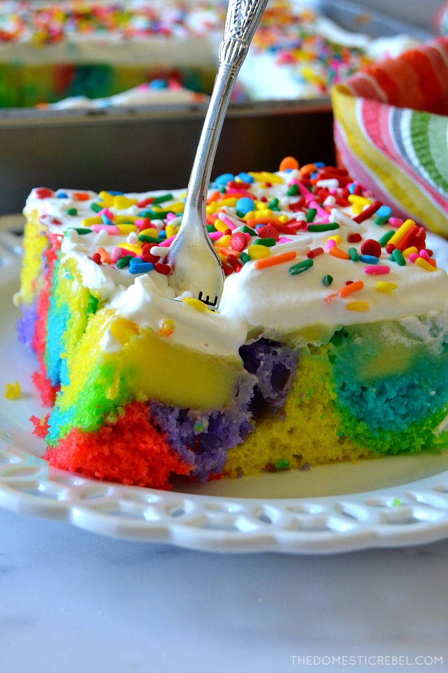 Rainbow Poke Cake slice on white plate with fork in the cake
