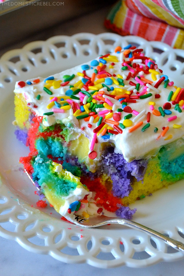 Rainbow Poke Cake on a white plate with a fork and a bite missing