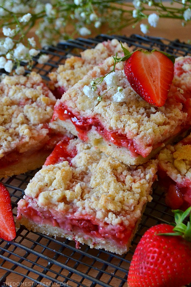 arrangement of strawberry crumble bars on wire rack with fresh berries and white flowers
