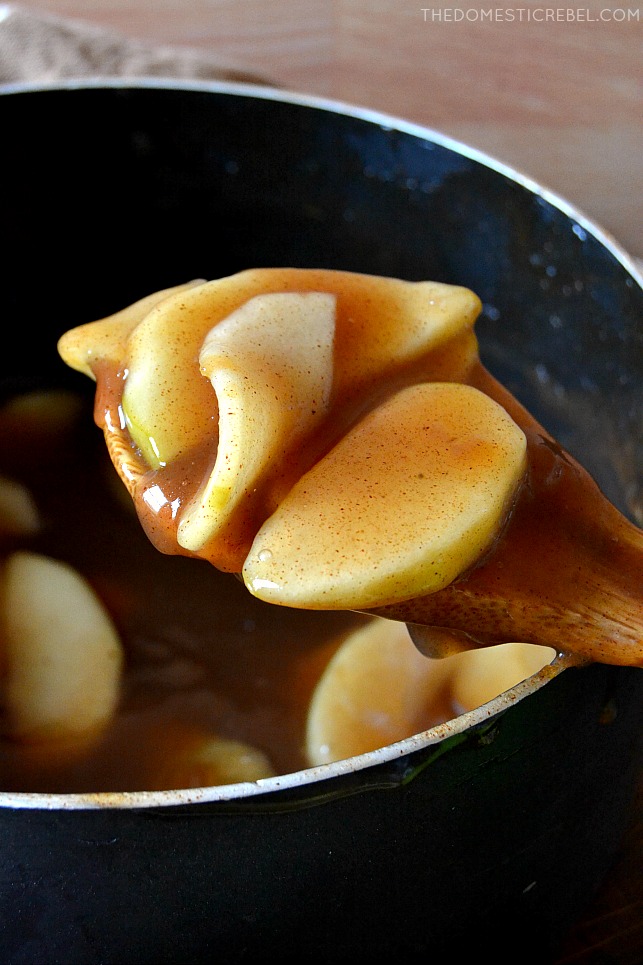 Closeup of wooden spoon holding some apple pie filling over a black pot