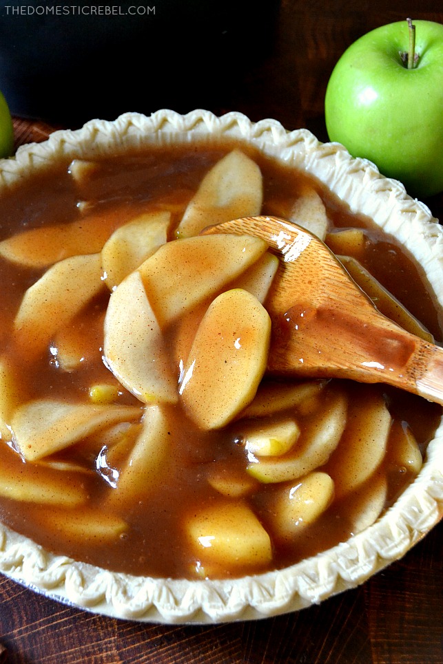 Apple pie filling in an unbaked pie crust with a wooden spoon and a green apple