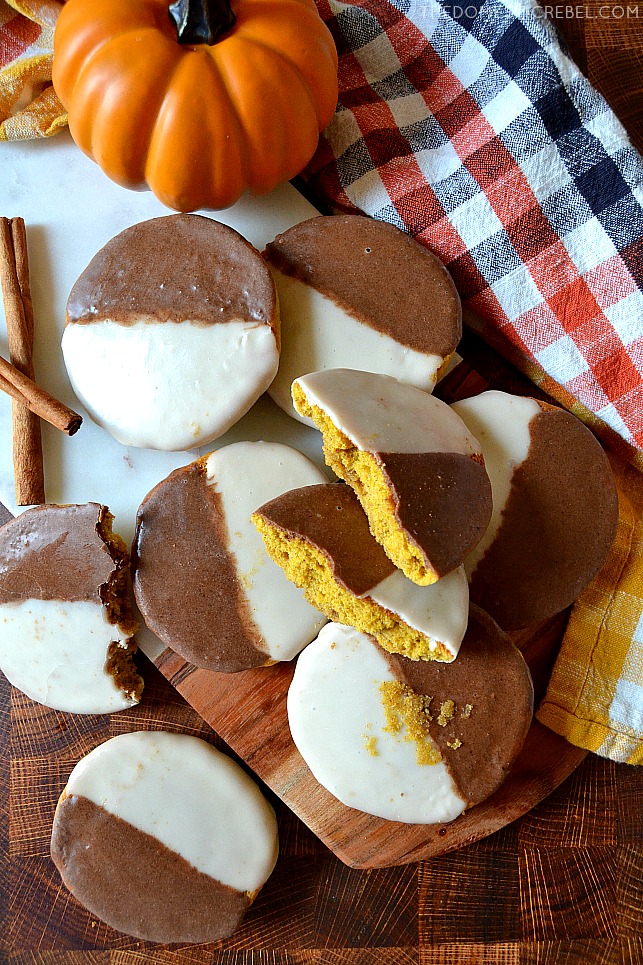 Scattered arrangement of pumpkin black and white cookies on a wooden cutting board
