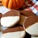 small pile of pumpkin black and white cookies with a pumpkin in the background