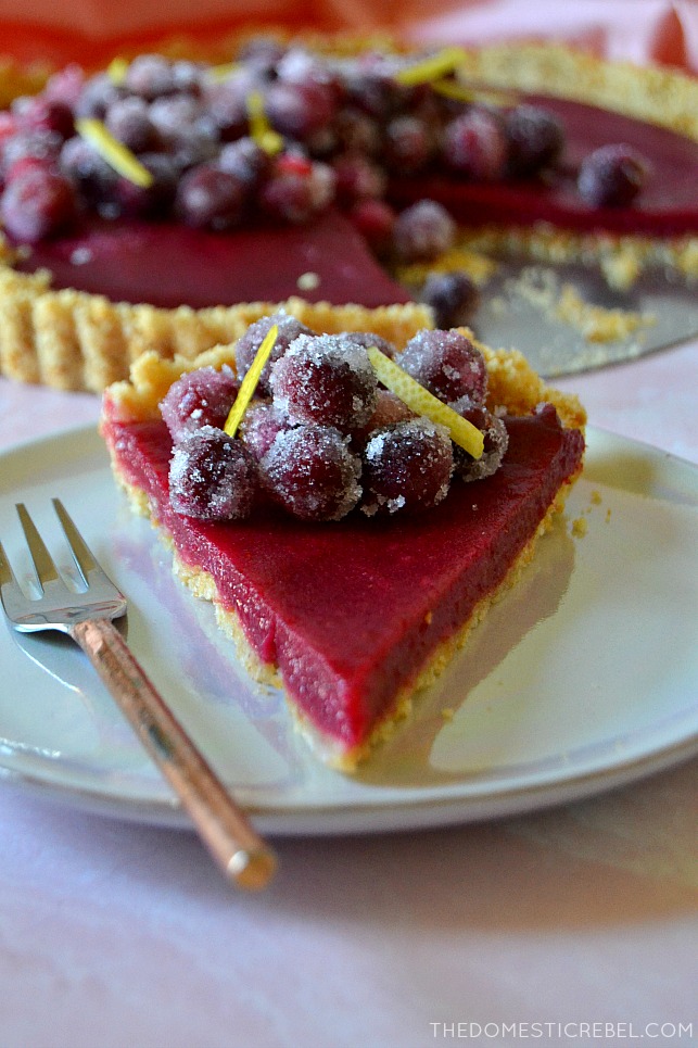 A slice of cranberry lemon tart on a purple plate with a gold fork