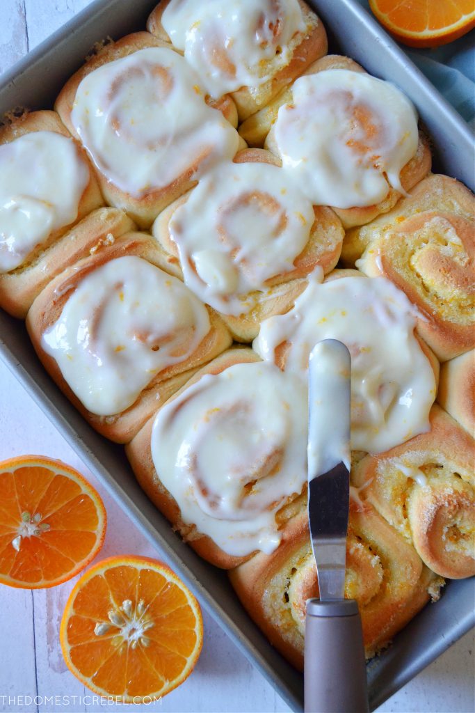 A pan filled with orange sweet rolls being frosted