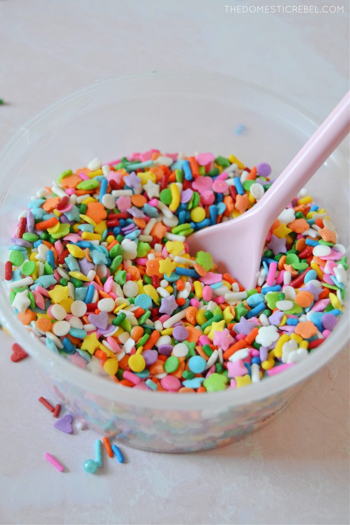 bowl of rainbow sprinkle blend with pink spoon inside 