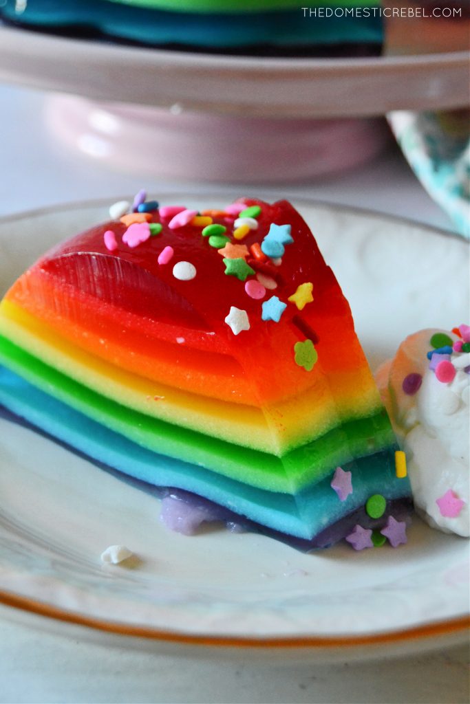 Rainbow jello mold slice on white plate with sprinkles