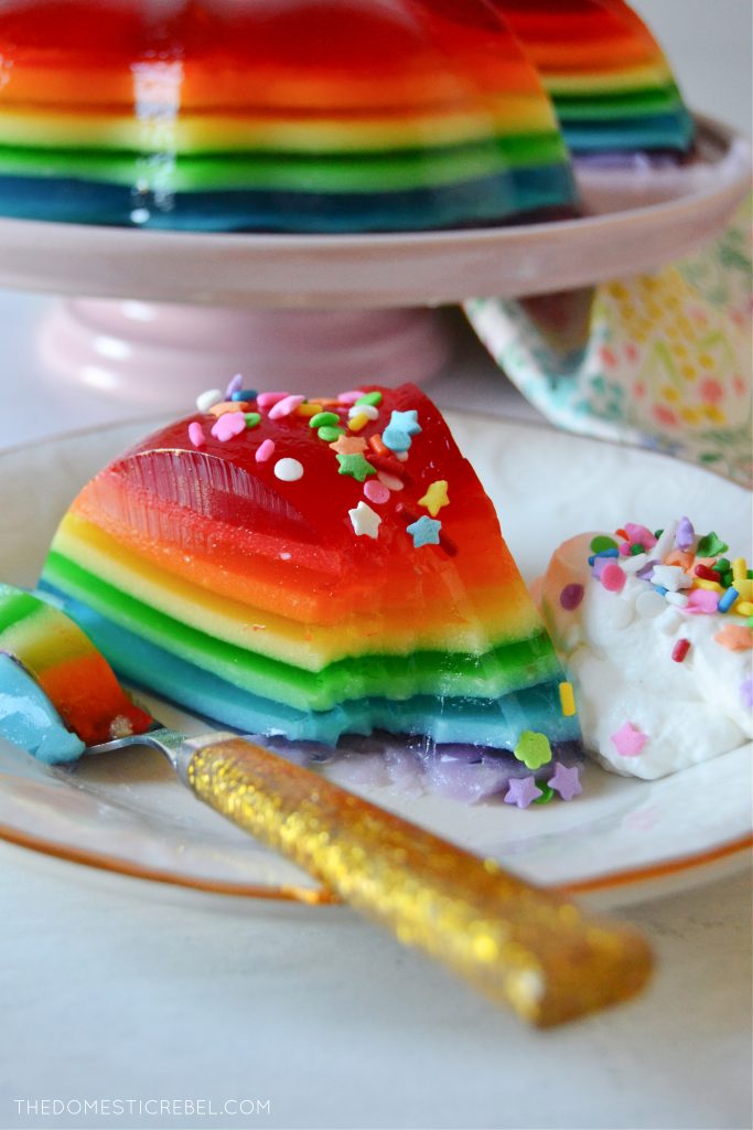 Rainbow jello mold slice on white plate with a bite missing