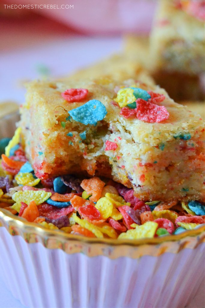 Closeup of a fruity pebble blondie with a bite missing in a bowl of cereal