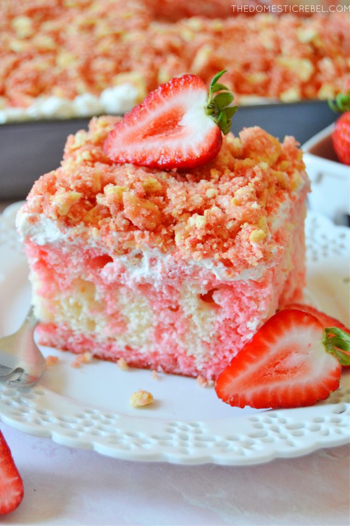 strawberry crunch poke cake slice with a fresh strawberry on a plate