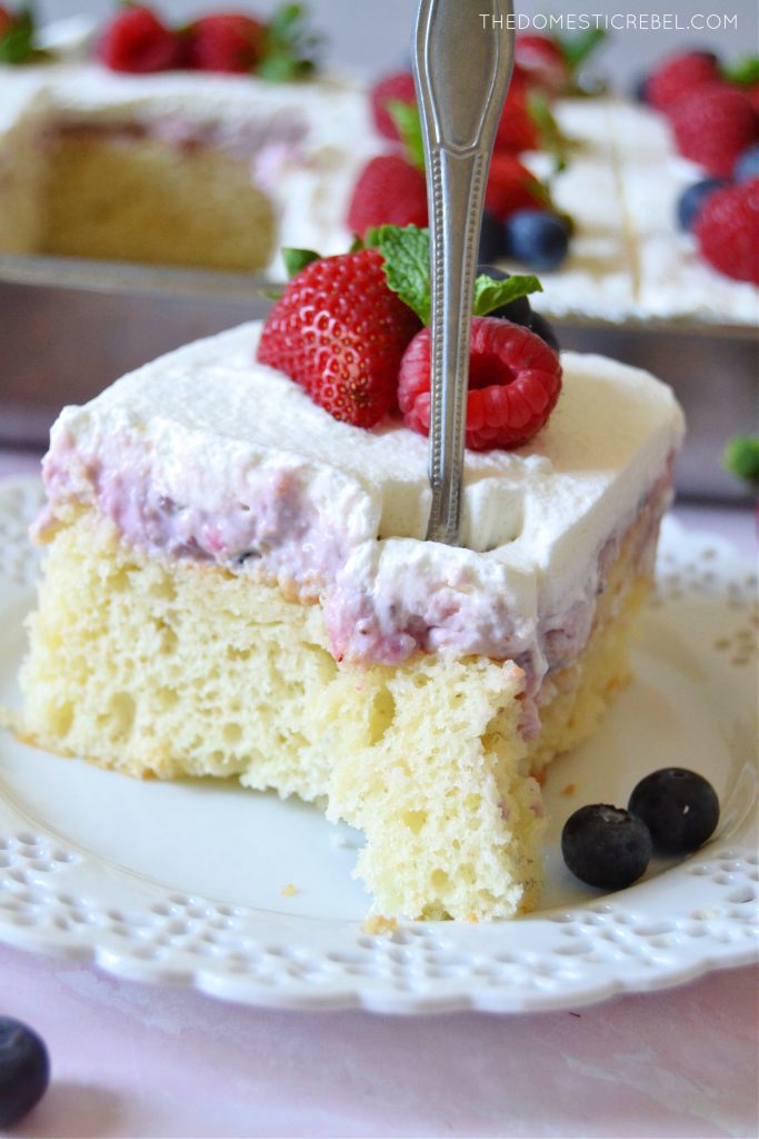 slice of berries and cream poke cake with a fork through it 