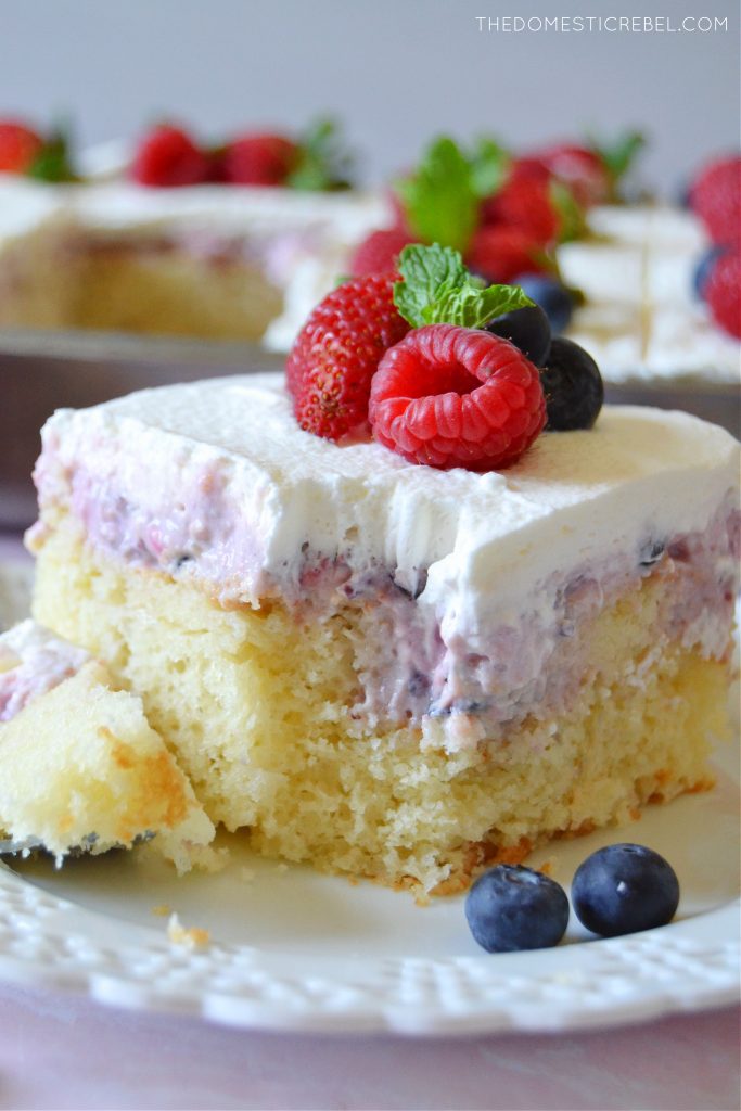 closeup of berries and cream poke cake with a bite missing