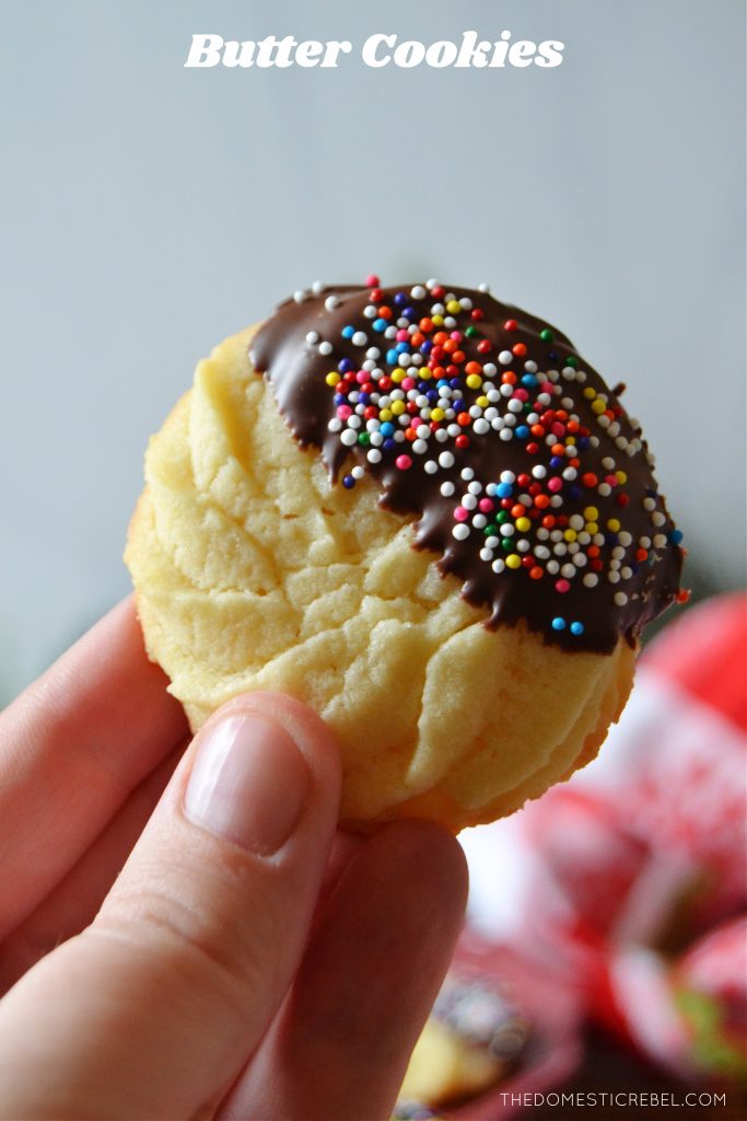 author holding a butter cookie dipped in chocolate and rainbow sprinkles