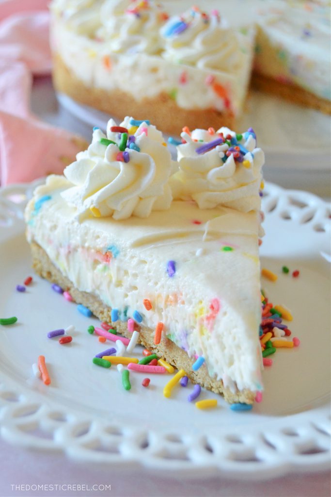 a slice of cake batter cheesecake on a white lacy plate with sprinkles