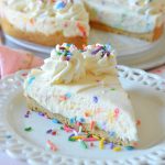 a piece of cake batter confetti cheesecake on a lacy white plate with sprinkles