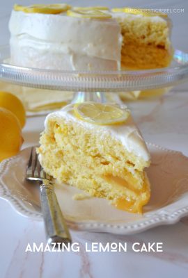 a piece of lemon cake on a white plate with the rest of the lemon layer cake in the background on a cake stand