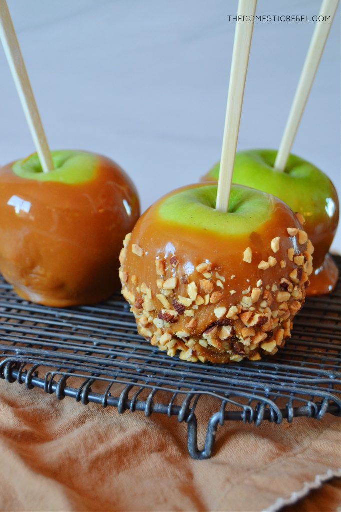 three assorted caramel apples on a black wire rack and brown cloth