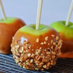 a closeup shot of a peanut caramel apple on a black baking rack with 2 caramel apples in the background
