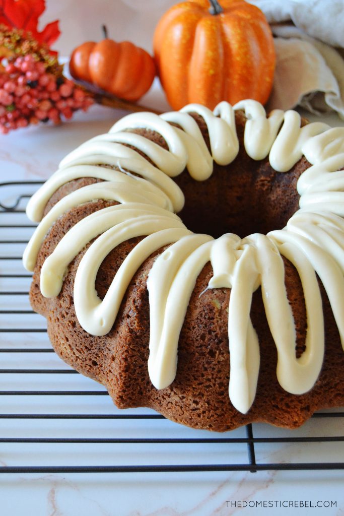 a close-up image of the entire pumpkin bundt cake iced on a black wire rack with mini faux pumpkins in the background