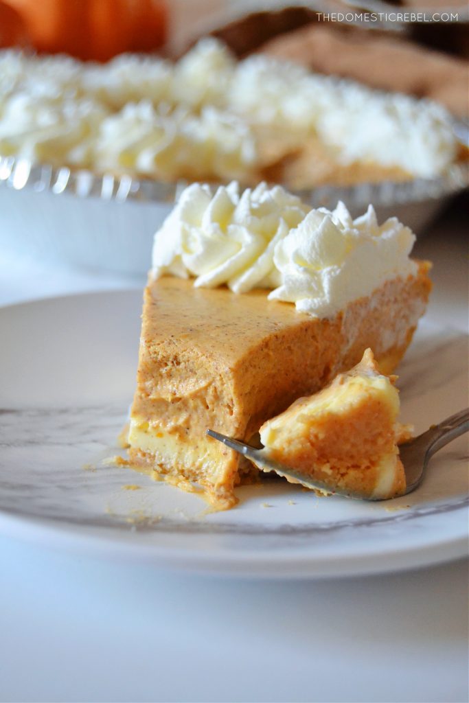 closeup of a pumpkin pie cheesecake on a white marble plate with a bite missing from the cheesecake slice