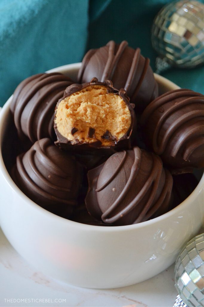 a bowl full of peanut butter balls, one has a bite missing from it