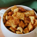 chex mix in a white handled bowl on a wooden board