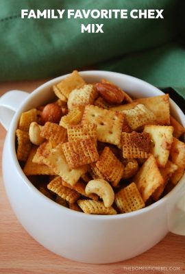 chex mix in a white handled bowl on a wooden board