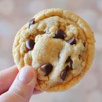 Photographer is holding a brown butter chocolate chip cookie against a light colored background.