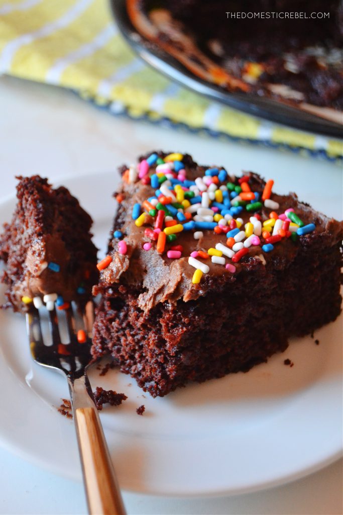 a piece of chocolate cake on a small white plate with a bite missing from the cake. a fork is resting on the plate with some cake on the fork.