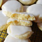 lemon meltaway cookies haphazardly arranged on a black wire baking rack. one of the cookies is split open to reveal the texture of the cookie.