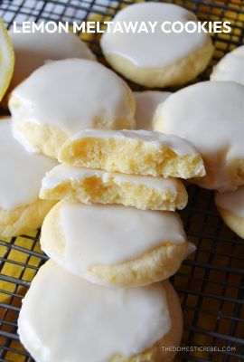 lemon meltaway cookies haphazardly arranged on a black wire baking rack. one of the cookies is split open to reveal the texture of the cookie.