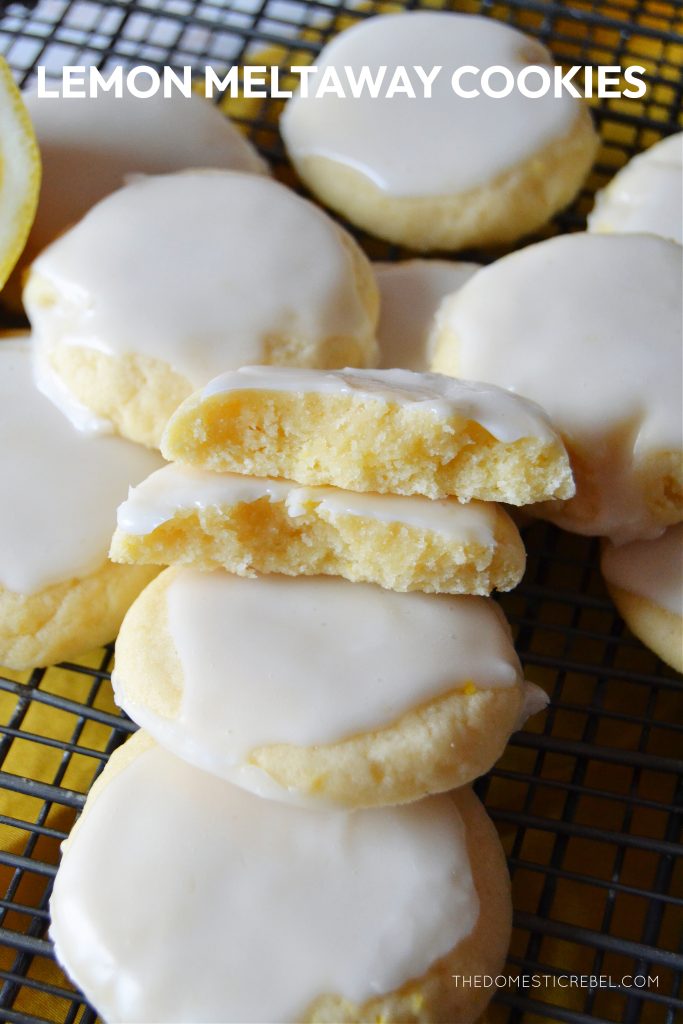 an arrangement of lemon meltaway cookies on a black wire rack. one of the cookies is split open to show the texture inside of the cookie.
