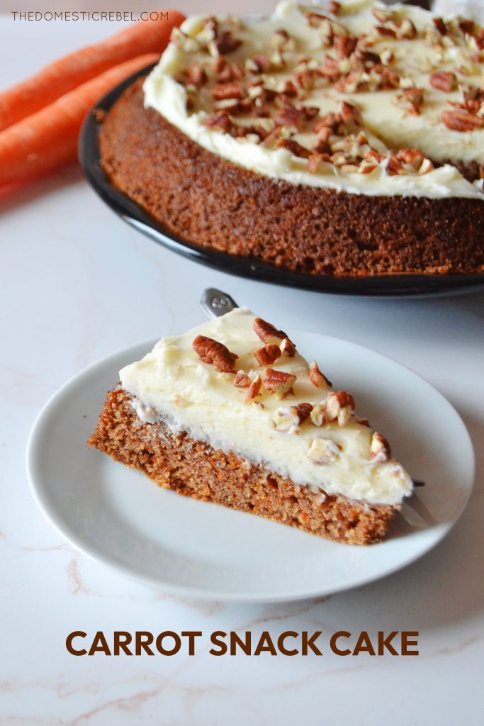 a piece of carrot snacking cake sits on a white plate. the remainder of the cake sits in the background on a black plate next to two carrots.