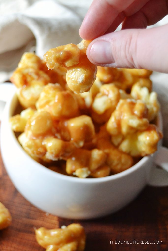 the author is holding a piece of caramel puff corn above a bowl of caramel puff corn.