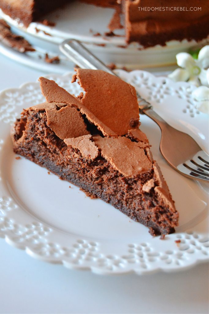 an aerial shot of a slice of flourless chocolate cloud cake on a white lacy plate with a fork resting on the plate.