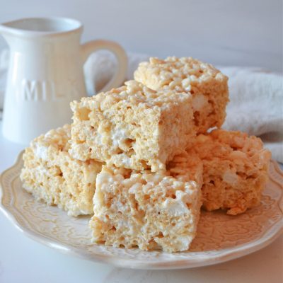 a little stack of brown butter vanilla rice krispy squares sits on a white lacy plate against a white background.