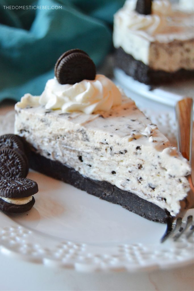 a closeup shot of a slice of oreo cheesecake on a white lacy plate with a few small oreo cookies on the plate as well.