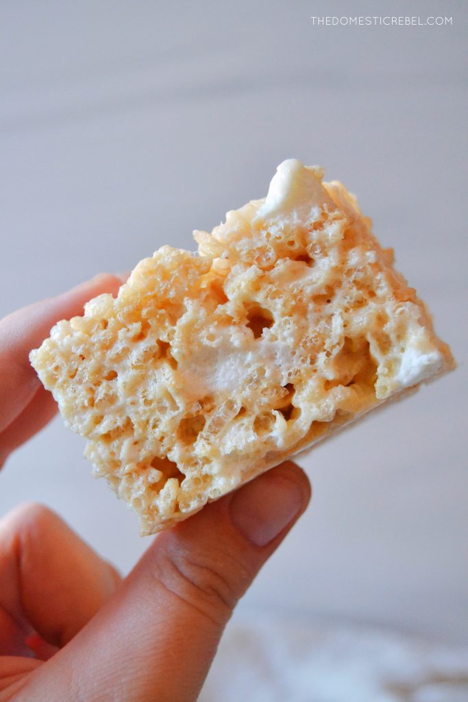 the author holds a single brown butter vanilla rice krispy treat square against a grainy light grey background. 