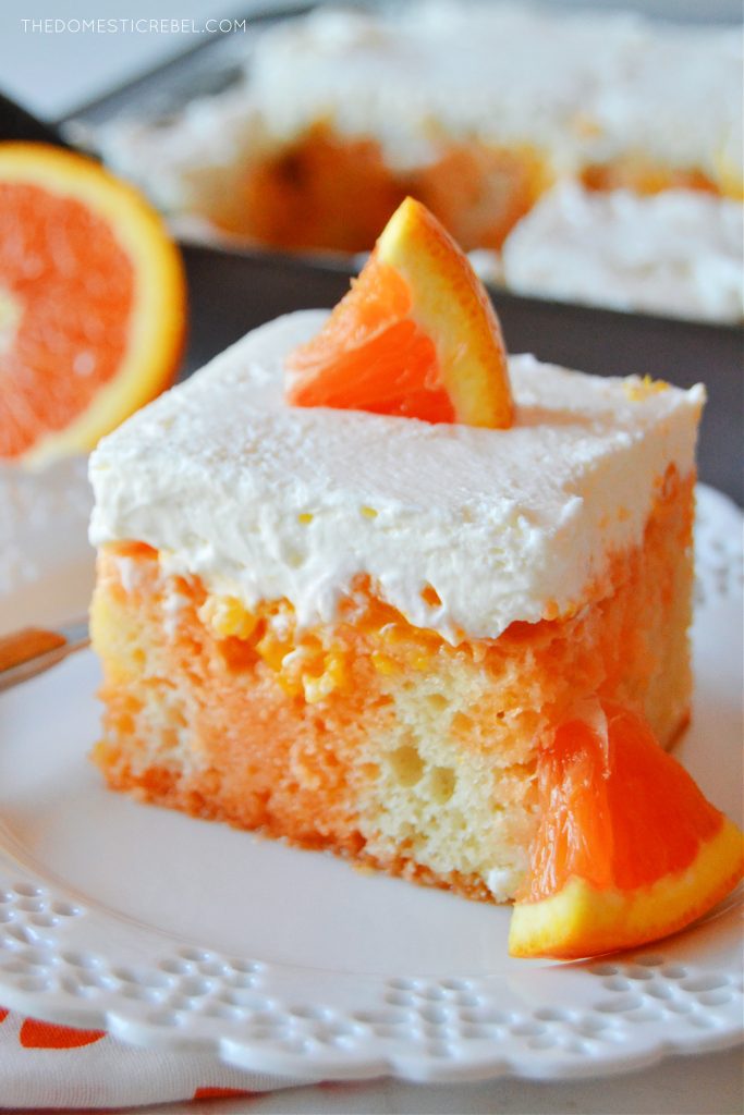 a closeup photo of a slice of orange creamsicle poke cake on a lacy white plate. an orange segment rests in the background. 