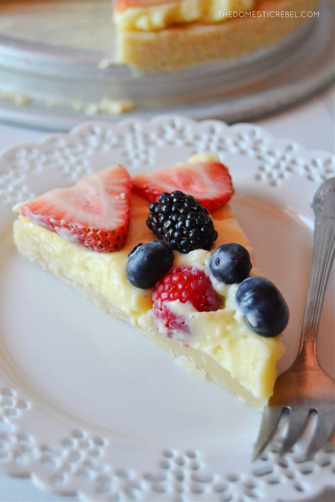 a slice of a homemade fruit tart on a lacy white plate with a silver fork resting next to it.