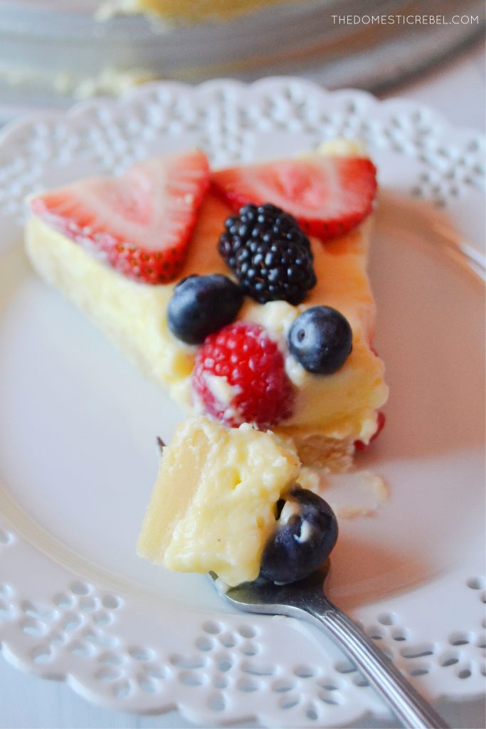 a slice of fruit tart on a white lacy plate with a bite missing out of the tart. a fork rests on the plate with a piece of the tart on the fork.